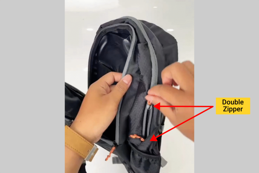 Tangan membuka ritsleting kompartemen utama tas Inflico BA325IFS, ditunjukkan tanda panah dan text overlay āDouble Zipperā.